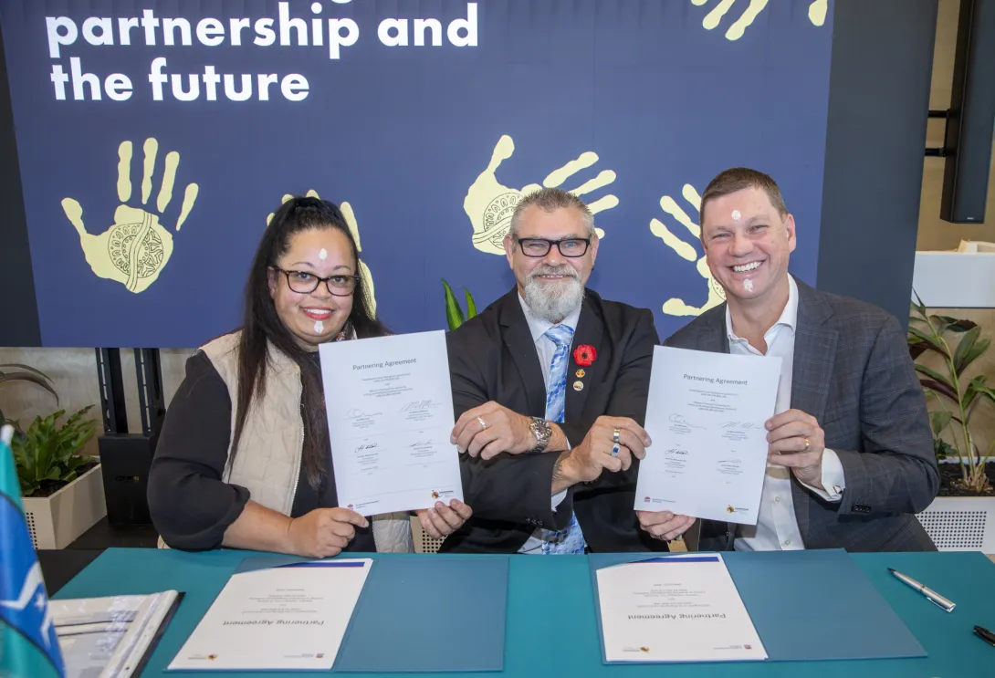 Three people shake hands with signed documents