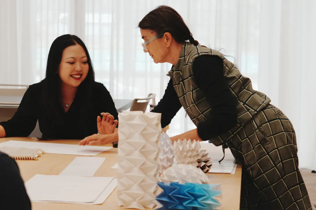 Two women in an art workshop with a paper sculpture on a desk