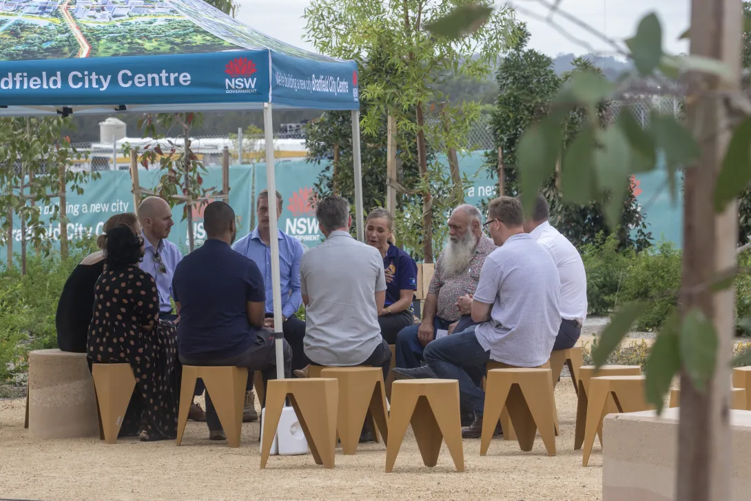Group sitting on stools for a yarning circle outside the First Building at Bradfield City